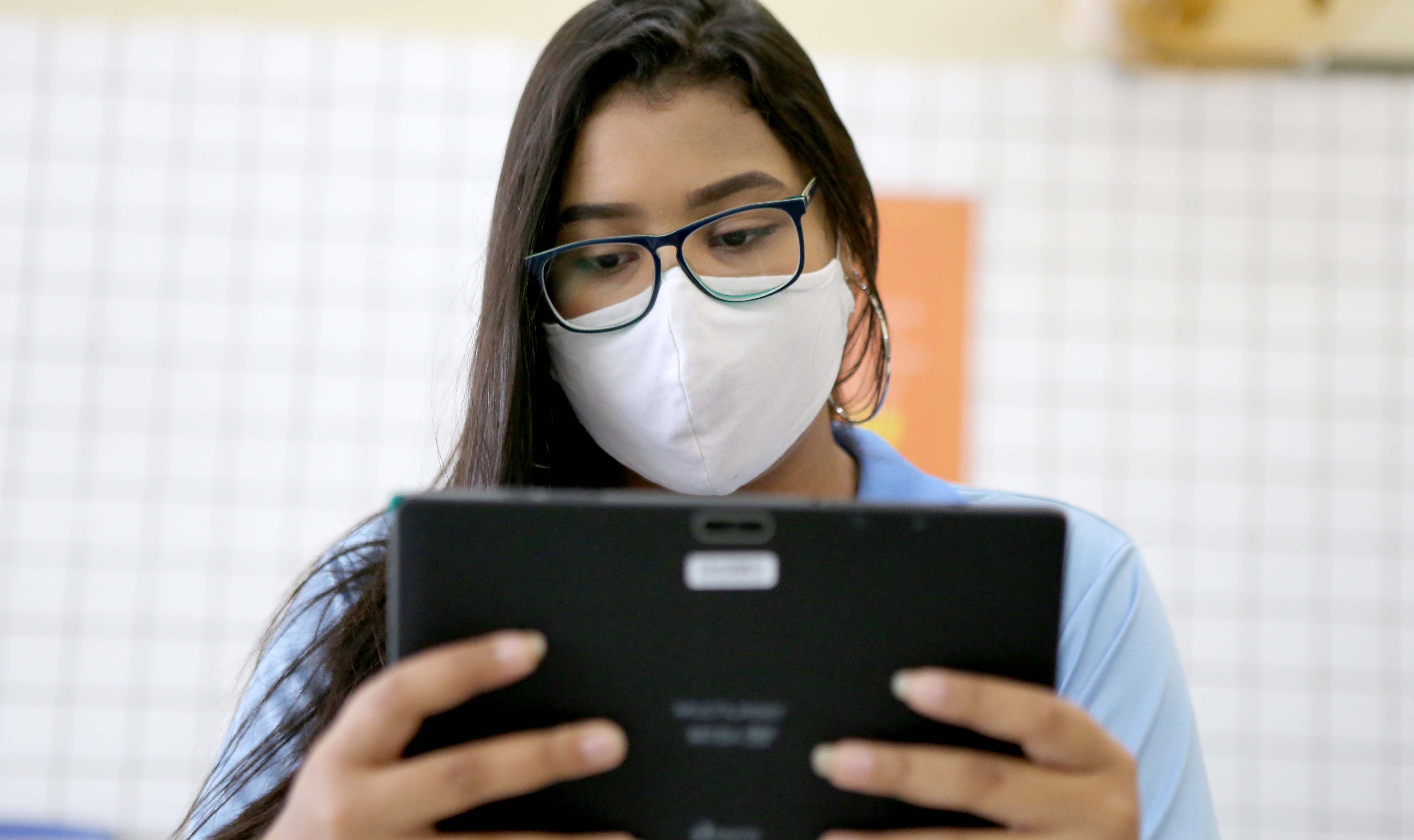 aluna com máscara segura um tablet